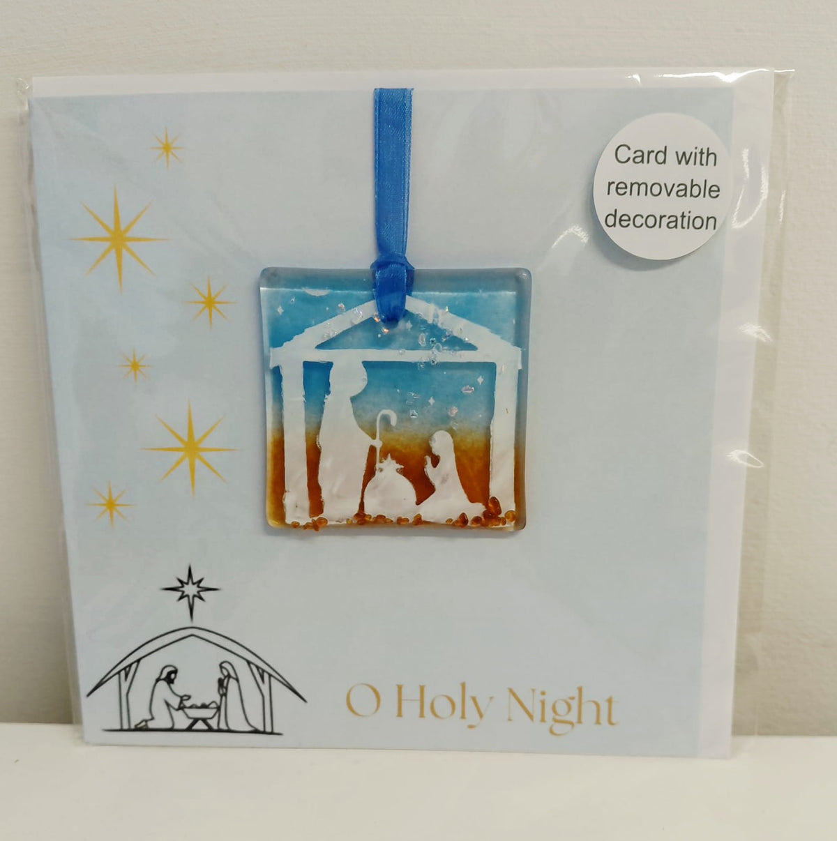 A packaged 'O Holy Night' glass nativity ornament card. The card is light blue with gold star graphics, a black line drawing of the nativity, and gold text.