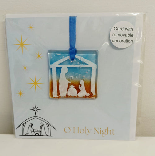 A packaged 'O Holy Night' glass nativity ornament card. The card is light blue with gold star graphics, a black line drawing of the nativity, and gold text.