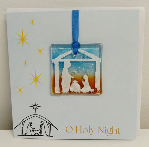 Handcrafted 6x6 inch “O Holy Night” Christmas greeting card featuring a detachable square fused glass nativity ornament with Joseph, Mary, baby Jesus in a manger silhouette against a sky blue and warm amber background.