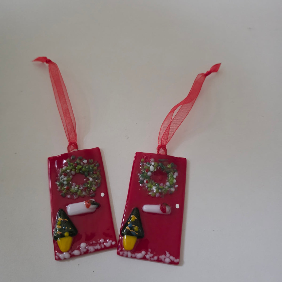 Handcrafted bright red fused glass festive front door tree ornament measuring 7x4cm, decorated with a textured wreath, letterbox, doorknob, potted mini Christmas tree, and snow dusting on a red hanging ribbon.